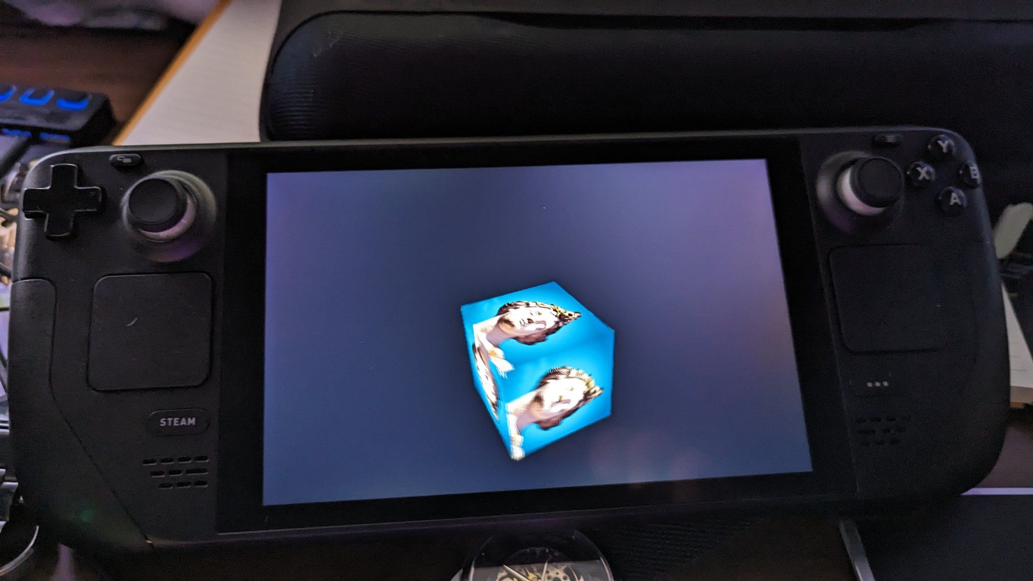 A textured cube on a black ground running on a Steam Deck. The cube would be spinning if this was animated.